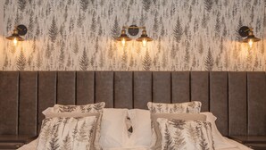 A neatly made bed with a headboard, multiple pillows, and a wall with a forest pattern. - Thatched Eaves (Ringwood)