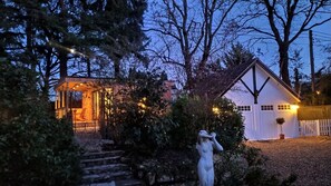 Une maison rustique avec un escalier en pierre menant à une porte en bois, entourée d’un feuillage dense et sous un ciel dégagé.