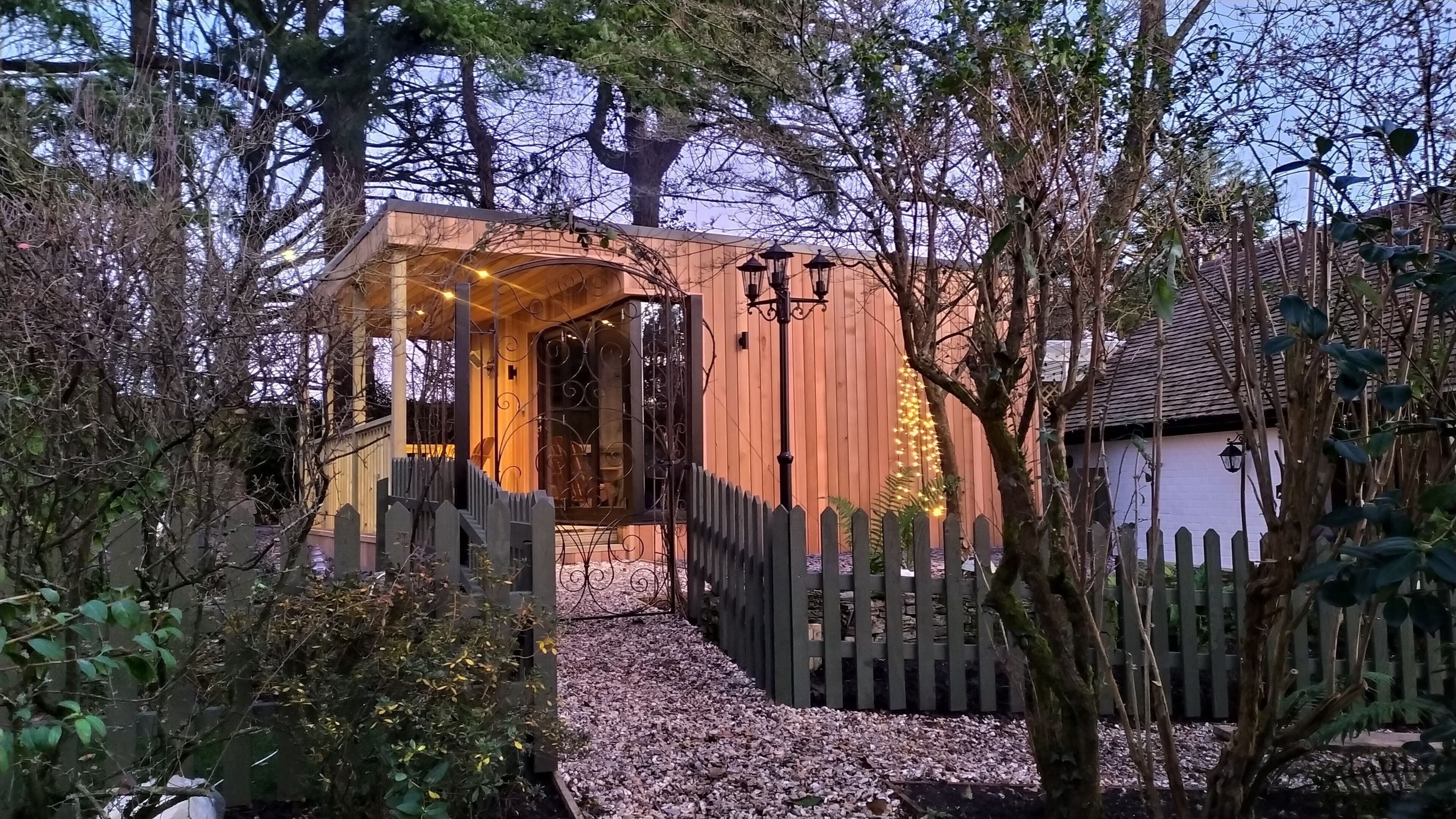 A wooden gazebo with a glass enclosure, surrounded by a gravel path and a wooden fence.