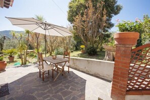 Una veranda all'aperto con tavolo e sedie in legno, un ombrellone grande e piante in vaso.