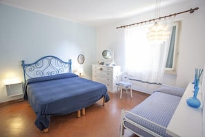 Un dormitorio con una cama, un escritorio, una silla y una pequeña mesa con un jarrón.