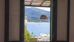 Ein offenes Fenster mit Blick auf eine Küstenlandschaft, einschließlich eines Gewässers und einer entfernten Bergkette.