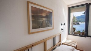 Ein Schlafzimmer mit einem Holz-Kopfteil, einem gerahmten Bild an der Wand, einem Nachttisch und einem Fenster mit Blick auf ein Gewässer und Berge.