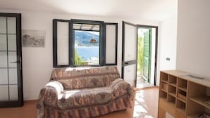 Ein Zimmer mit einer gemusterten Couch, einem Holzbodenregal und Blick auf eine Berglandschaft durch ein Fenster.