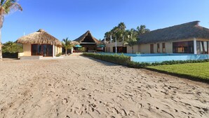 Ein Resort mit strohgedeckten Häusern, einem Schwimmbad und Palmen.