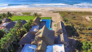 Ein Resort mit strohgedeckten Gebäuden, einem Schwimmbad und Blick auf den Strand.