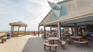 A wooden deck with picnic tables, a gazebo, and a restaurant named "The Quarter Deck" with a wave design. - Birdie's Beachfront I - The only Oceanfront Condo to be at Myrtle Beach Resort (Myrtle Beach)
