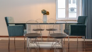 A dining area with a glass table, metal chairs, a white vase with flowers, and a window with curtains. - Chiado Patio Apartment (Lisboa)