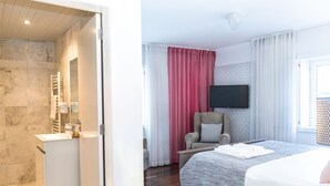 A hotel room with a bed, a chair, a TV, a bathroom with a sink, and a shower. - Chiado Patio Apartment (Lisboa)