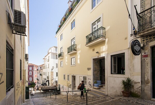 A narrow street with buildings on either side, a person walking, and a parked truck.