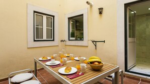 A breakfast table set with plates, croissants, fruit, and drinks, with two windows and a door in the background. - Chiado Patio Apartment (Lisboa)