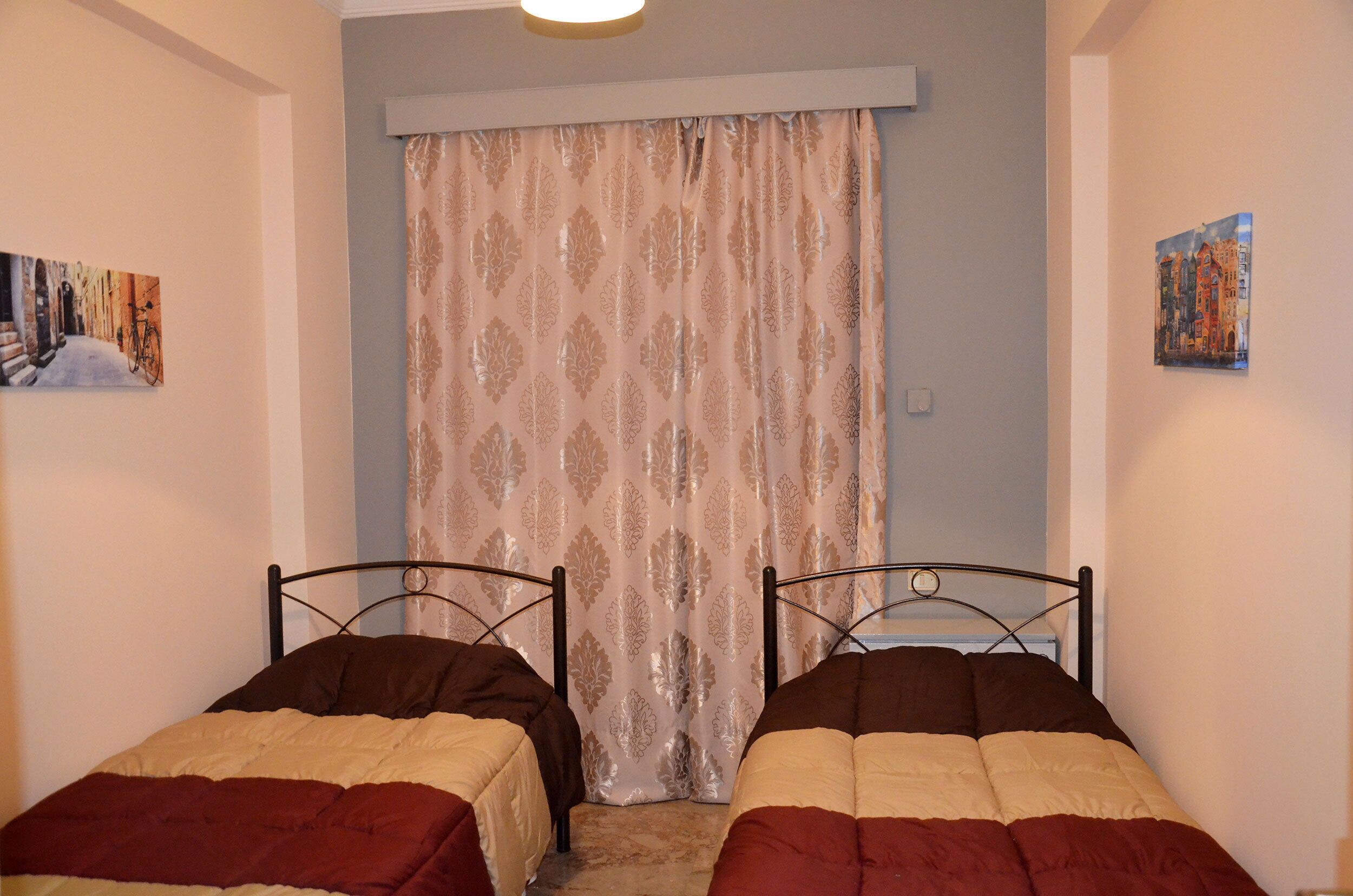 A bedroom with two single beds, a patterned curtain, and two wall-mounted paintings.