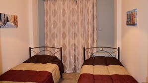 Une chambre avec deux lits simples, un rideau à motifs et deux tableaux accrochés au mur.