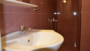 Une salle de bain avec un lavabo blanc, un miroir au-dessus, et un espace douche doté d’une porte en verre.
