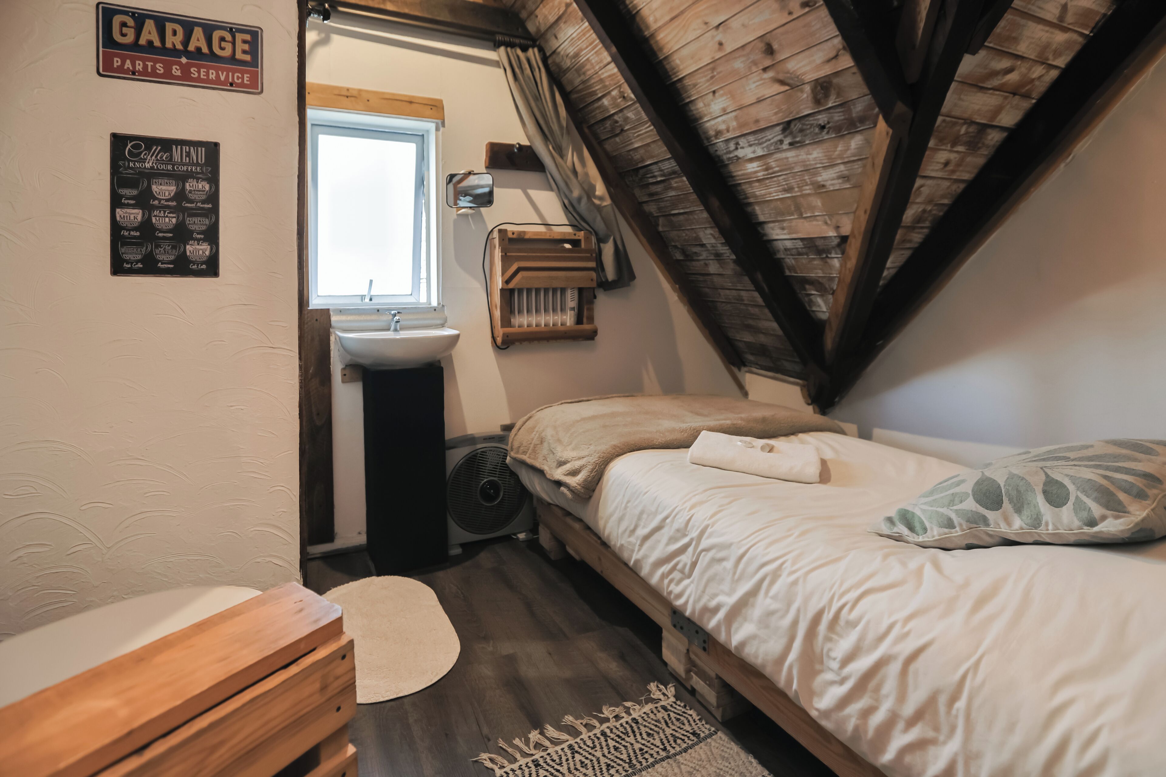 Camera da letto con soffitto in legno, un letto, un comodino, una cassettiera, una finestra e un cartello che indica un garage.
