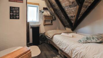 Camera da letto con soffitto in legno, un letto, un comodino, una cassettiera, una finestra e un cartello che indica un garage.