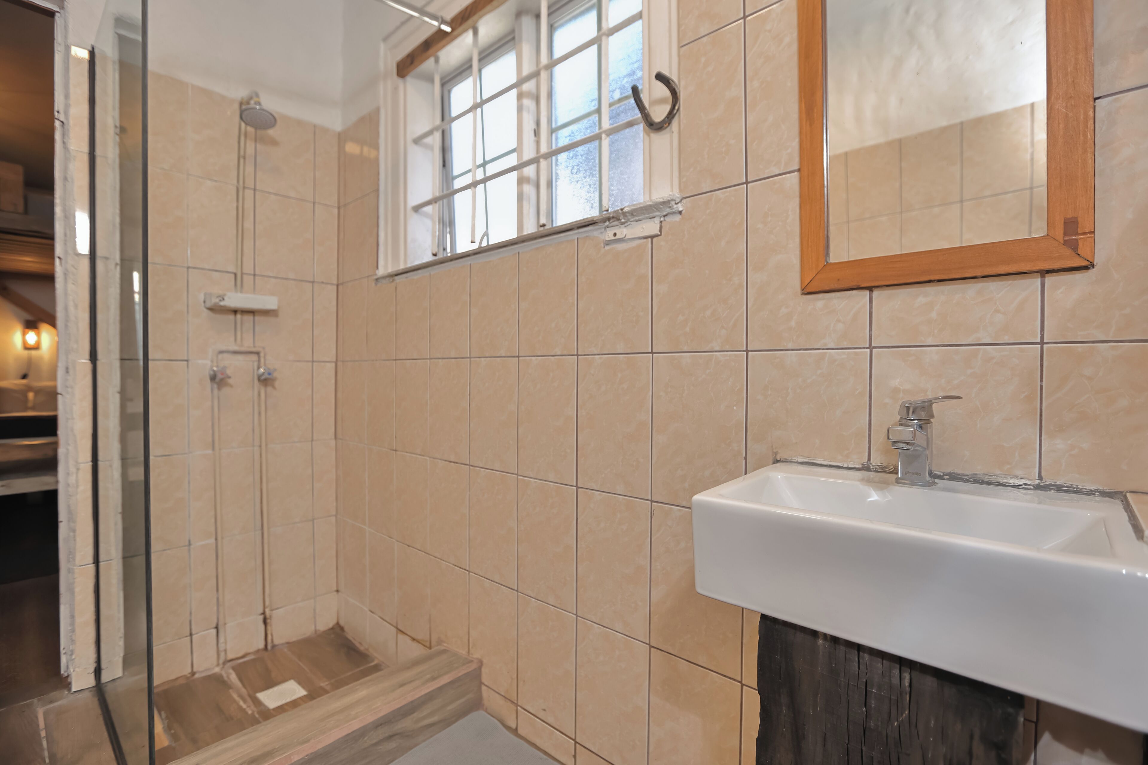 Een badkamer met een douche, wastafel en raam.