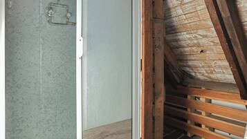A shower with a glass door, wooden beams, and a wooden floor in a room with a sloped ceiling.
