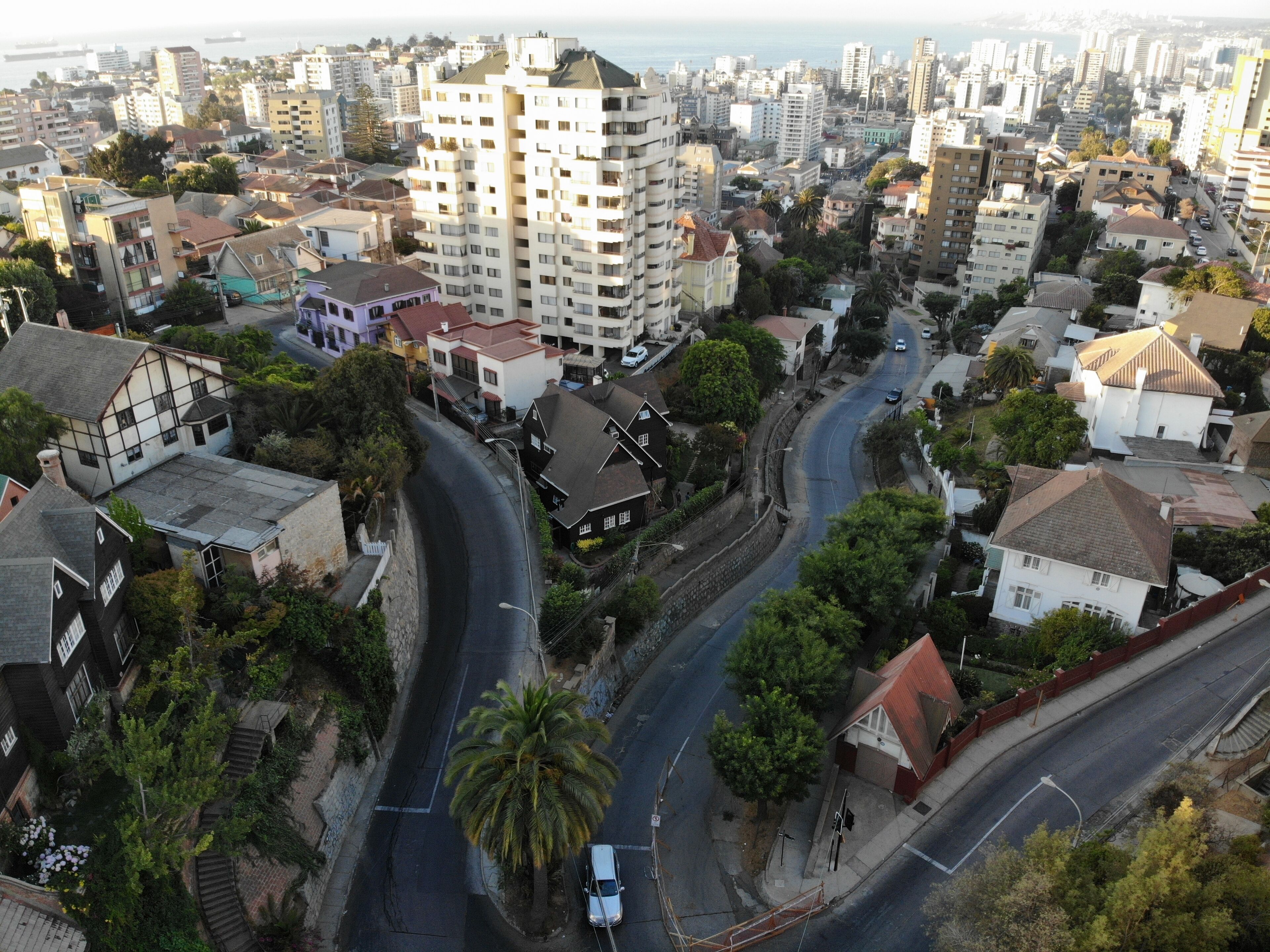 Vue aérienne d’un quartier résidentiel où se côtoient des bâtiments modernes et traditionnels, notamment un imposant immeuble à plusieurs étages et une route sinueuse.