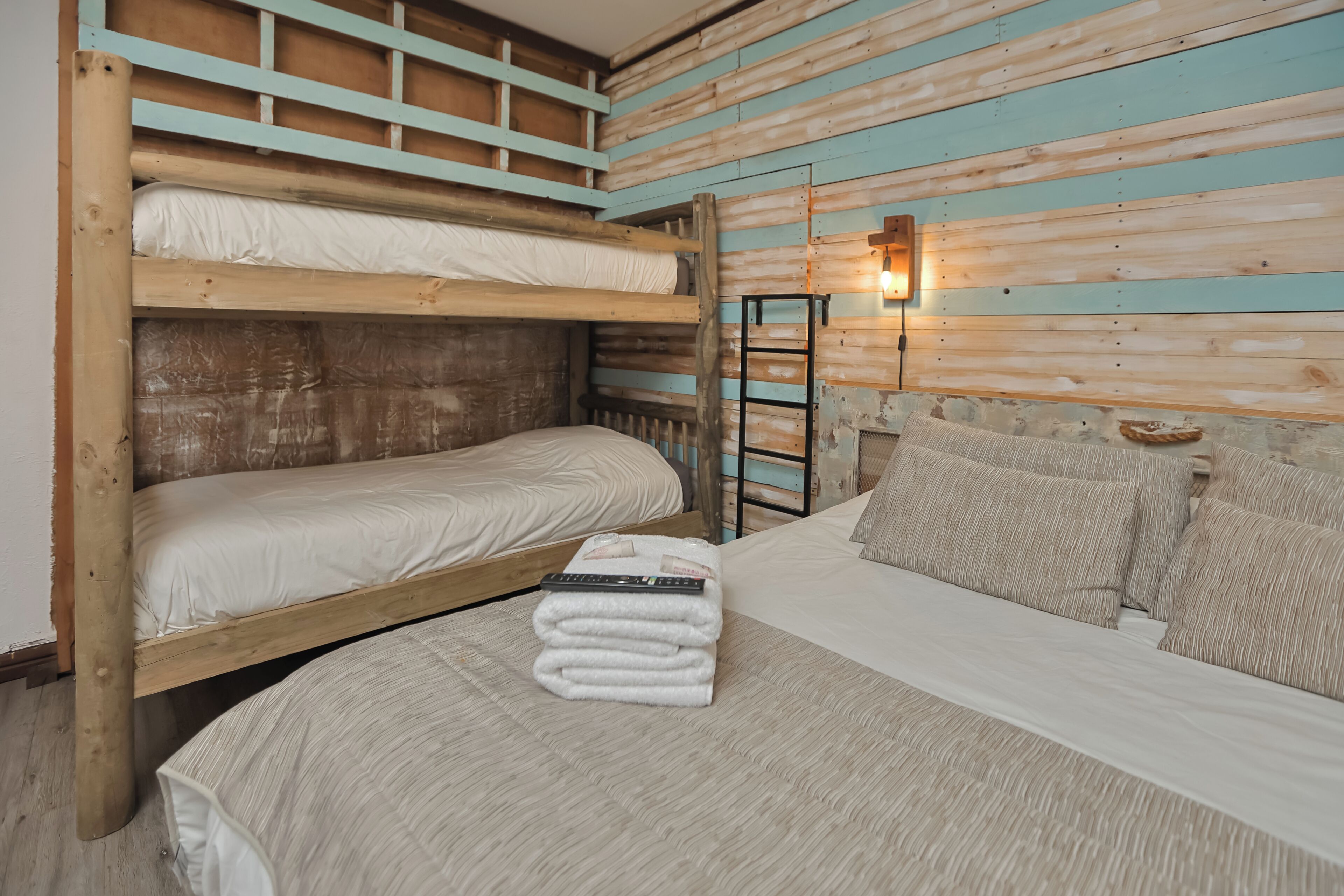 A bunk bed room with a wooden headboard, a small ladder, and a wall-mounted light fixture.