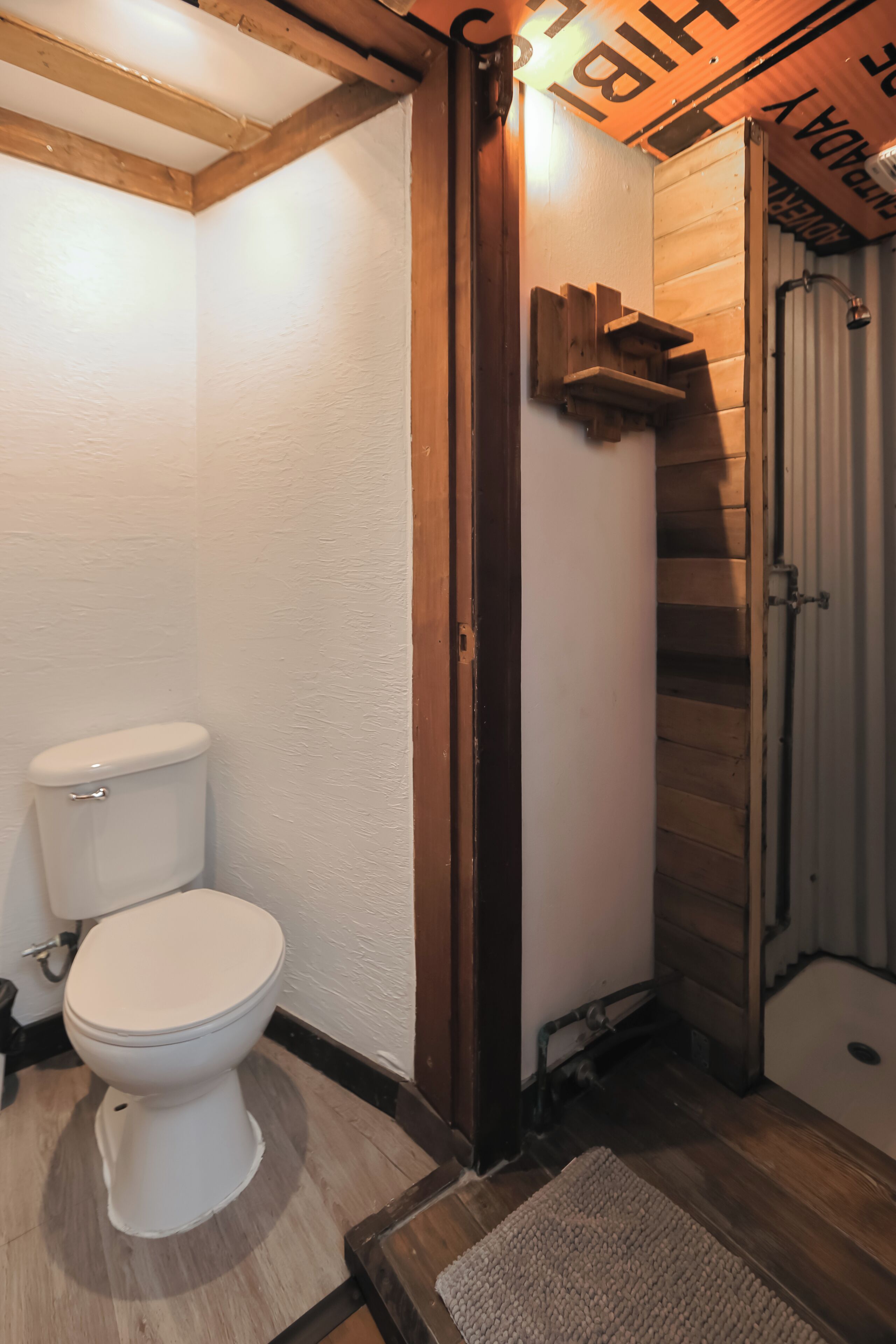 A bathroom with a white toilet, wooden floor, and a wooden door.