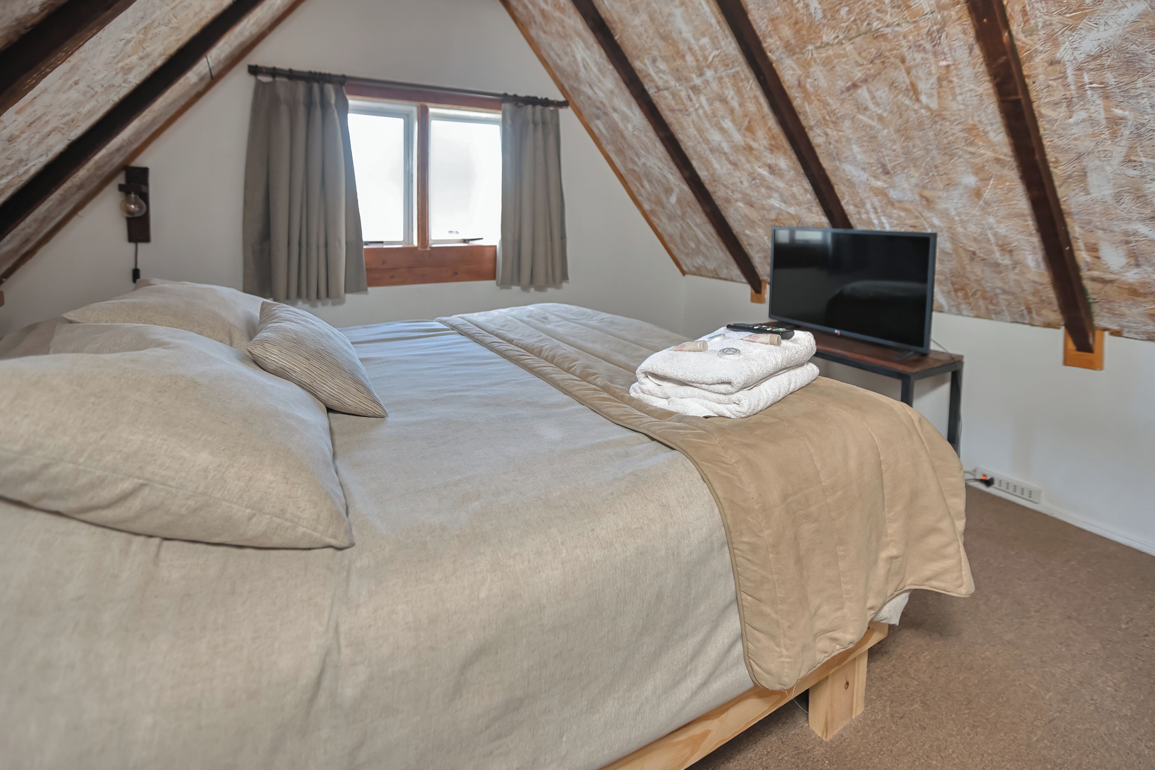 Ein Schlafzimmer mit Bett, Kissen, einem Fernseher auf einem Holzboden und einem Fenster mit Vorhängen.