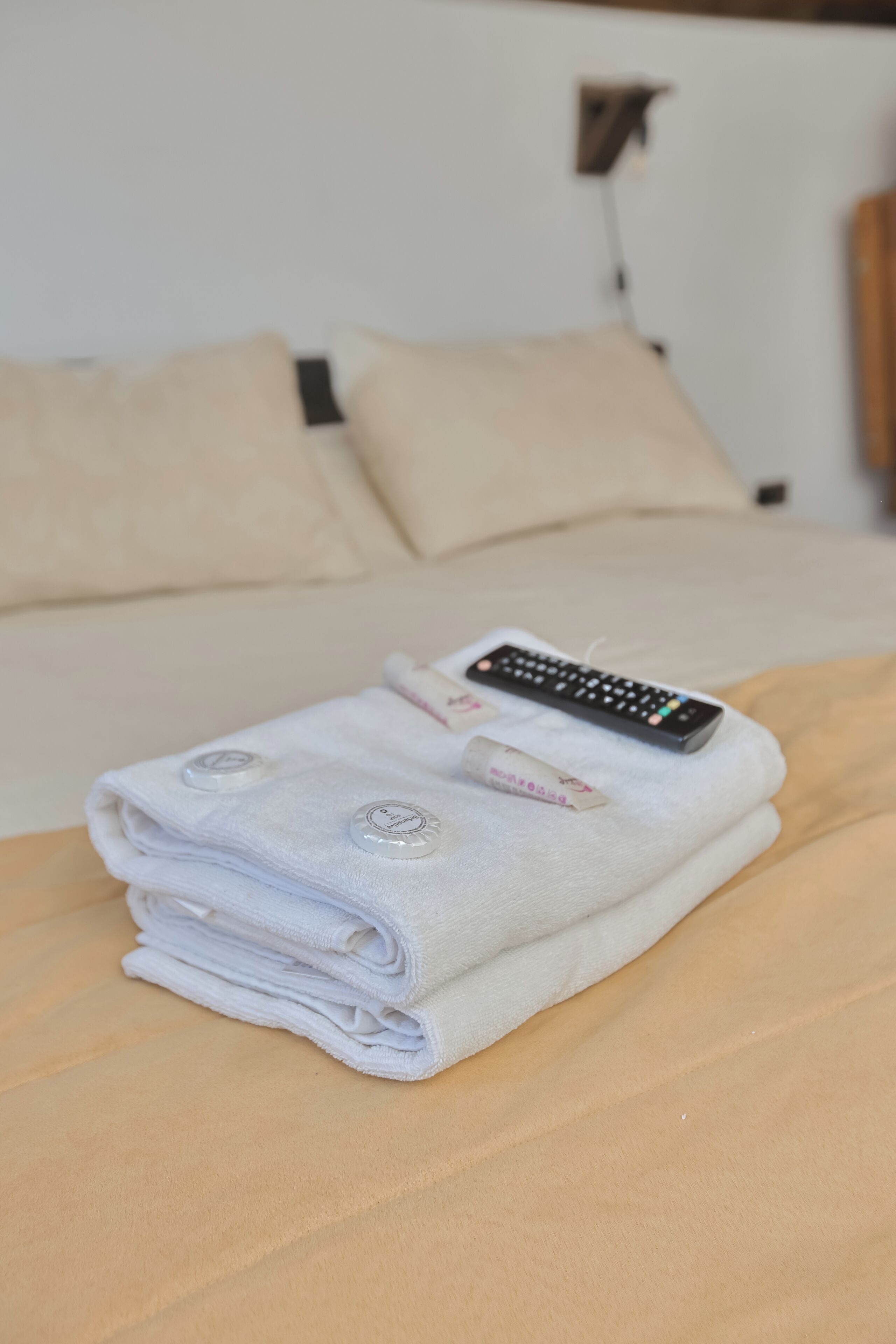 A neatly folded white towel with a remote control on a bed.