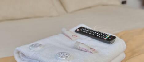 A neatly folded white towel with a remote control on a bed.