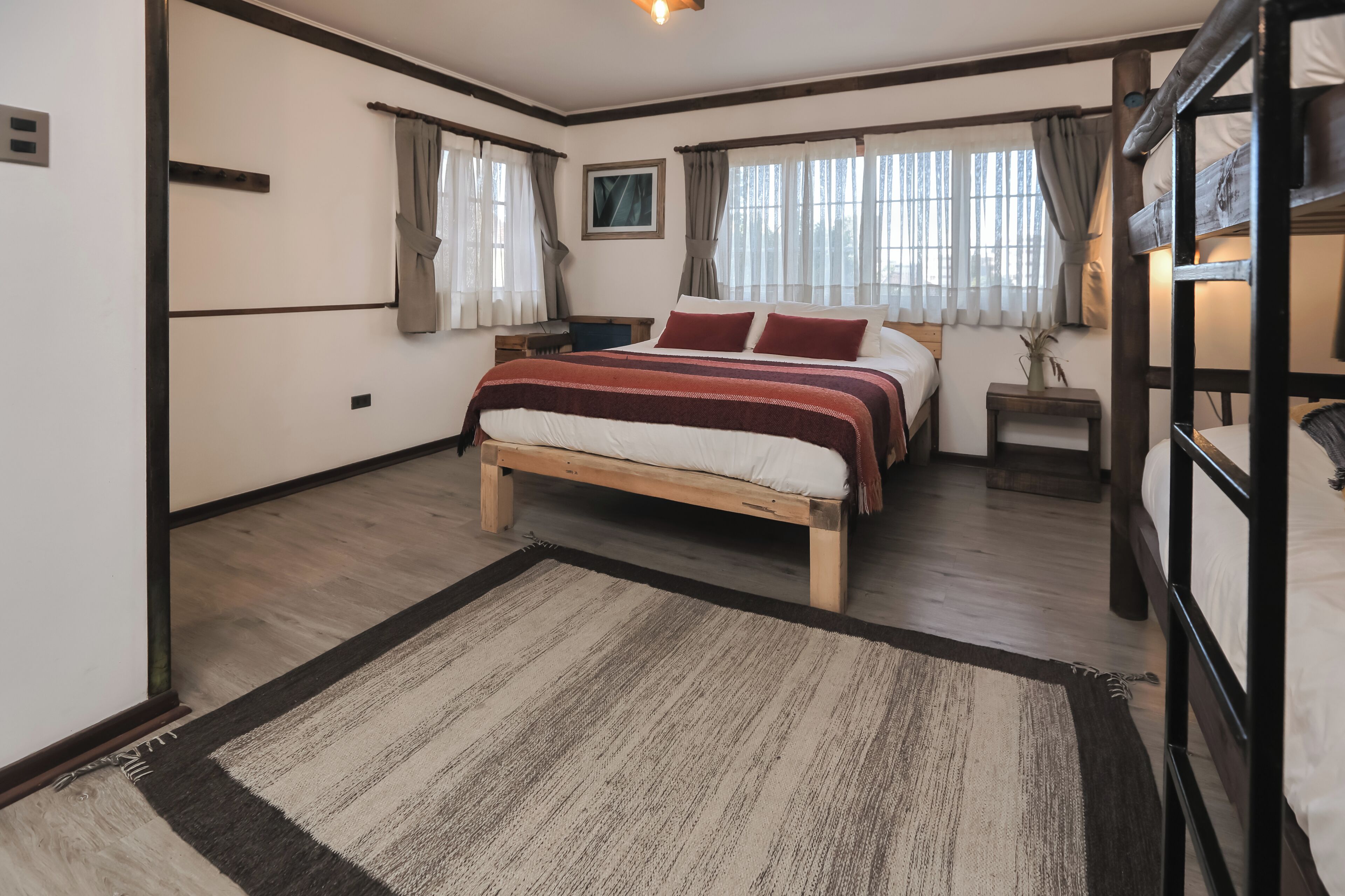 A bedroom with a wooden bed, a bedside table, a nightstand, and a window with curtains.