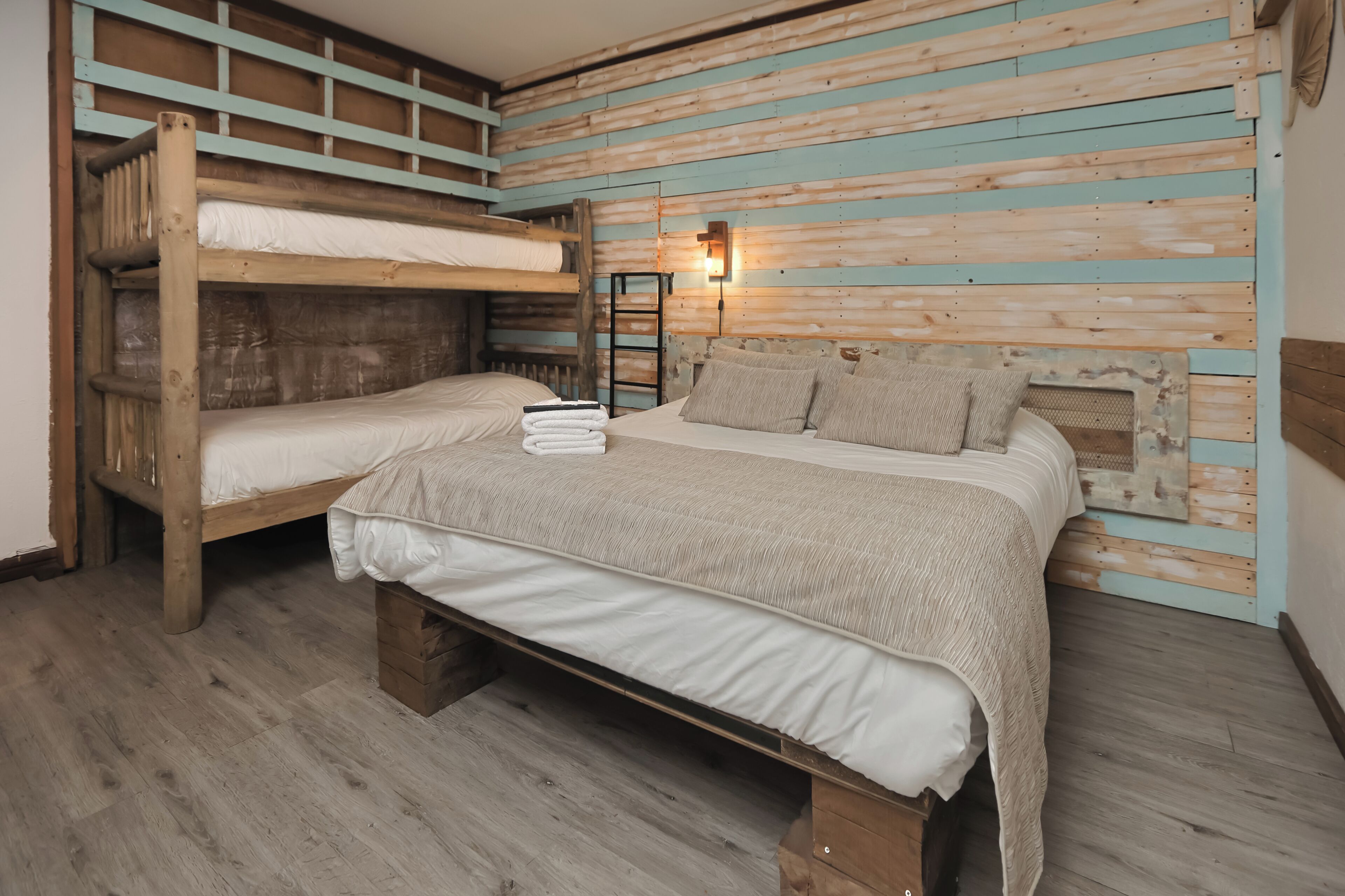 Habitación con literas, suelo de madera, luz empotrada en la pared y una escalera.