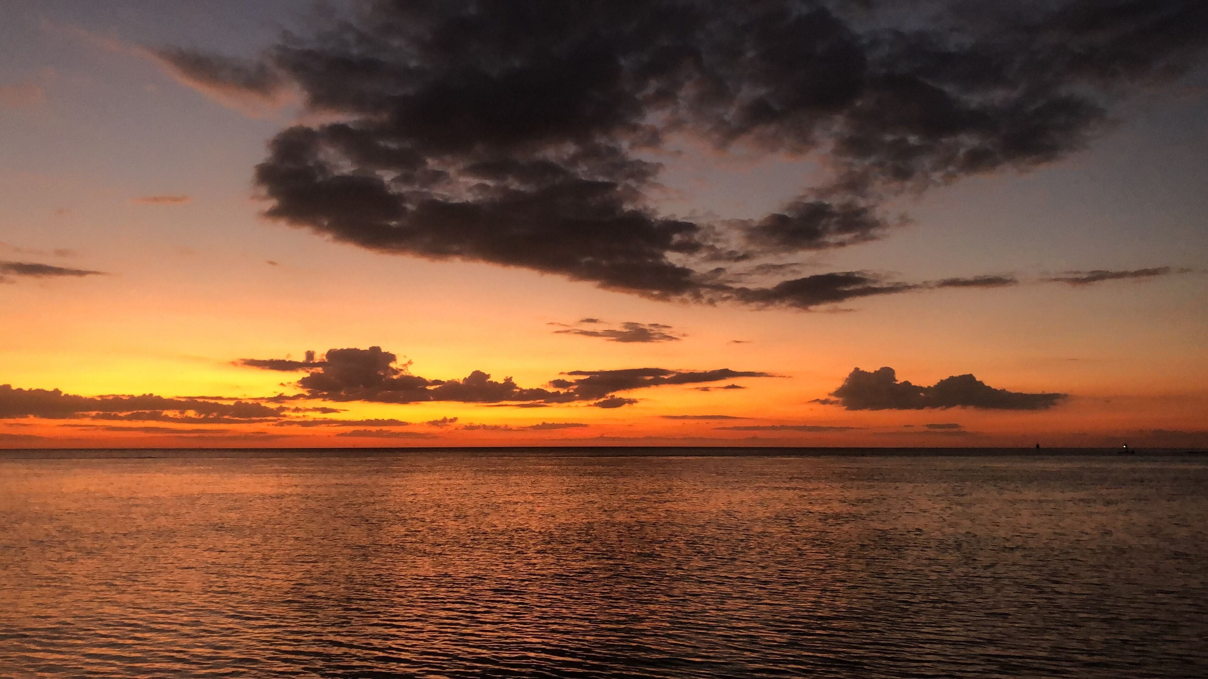 Een zonsondergang boven een rustige zee met een heldere horizon.
