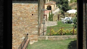 Un edificio de piedra con techo de tejas, un pequeño jardín con un paraguas blanco y vistas a una ladera.
