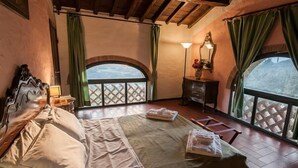 Un dormitorio con una cama grande, una mesita de noche, una lámpara y vistas al exterior a través de una ventana.