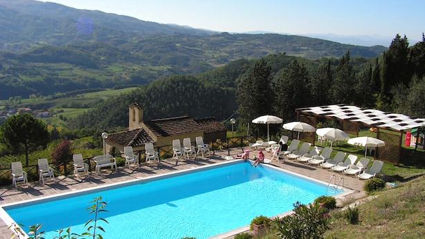 Una piscina con sillas de descanso y sombrillas, rodeada de follaje y colinas.