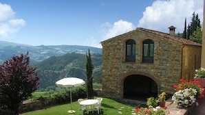 Un edificio de piedra con un pequeño patio, una sombrilla blanca y una mesa con sillas.