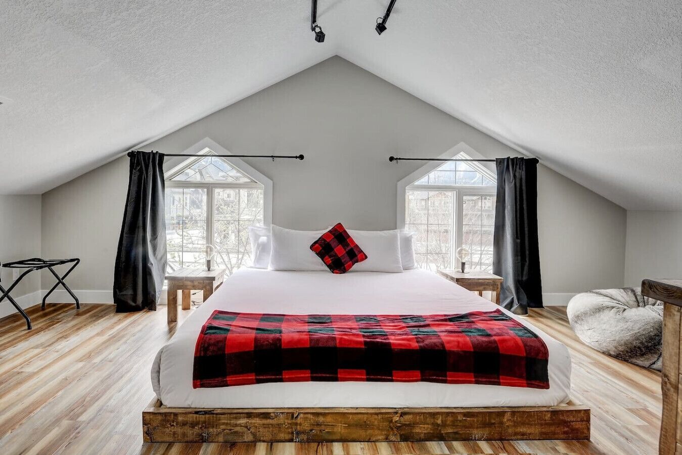 Une chambre avec un plafond en pente, un lit recouvert d’une couverture à carreaux rouges et noirs, des oreillers blancs et une tête de lit en bois.