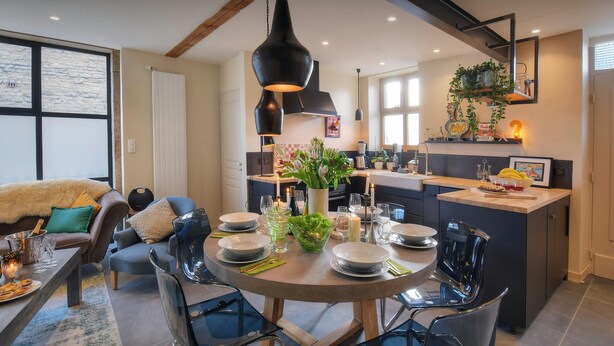 Een moderne keuken met een eethoek, met een ronde tafel met stoelen, een hanglamp en een vast kookeiland met spoelbak.