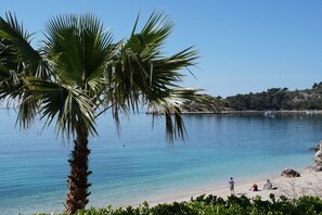 A beach with clear blue water, palm trees, and people relaxing on the shore. - PENDO 1 apartment with sea view, near beach (Mlini)