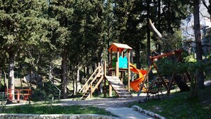 Un parc infantil amb una estructura de joc de fusta, tobogan i cadira de balanceig.