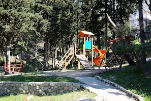 Un parque infantil con una estructura de madera para escalar, un tobogán y columpios.