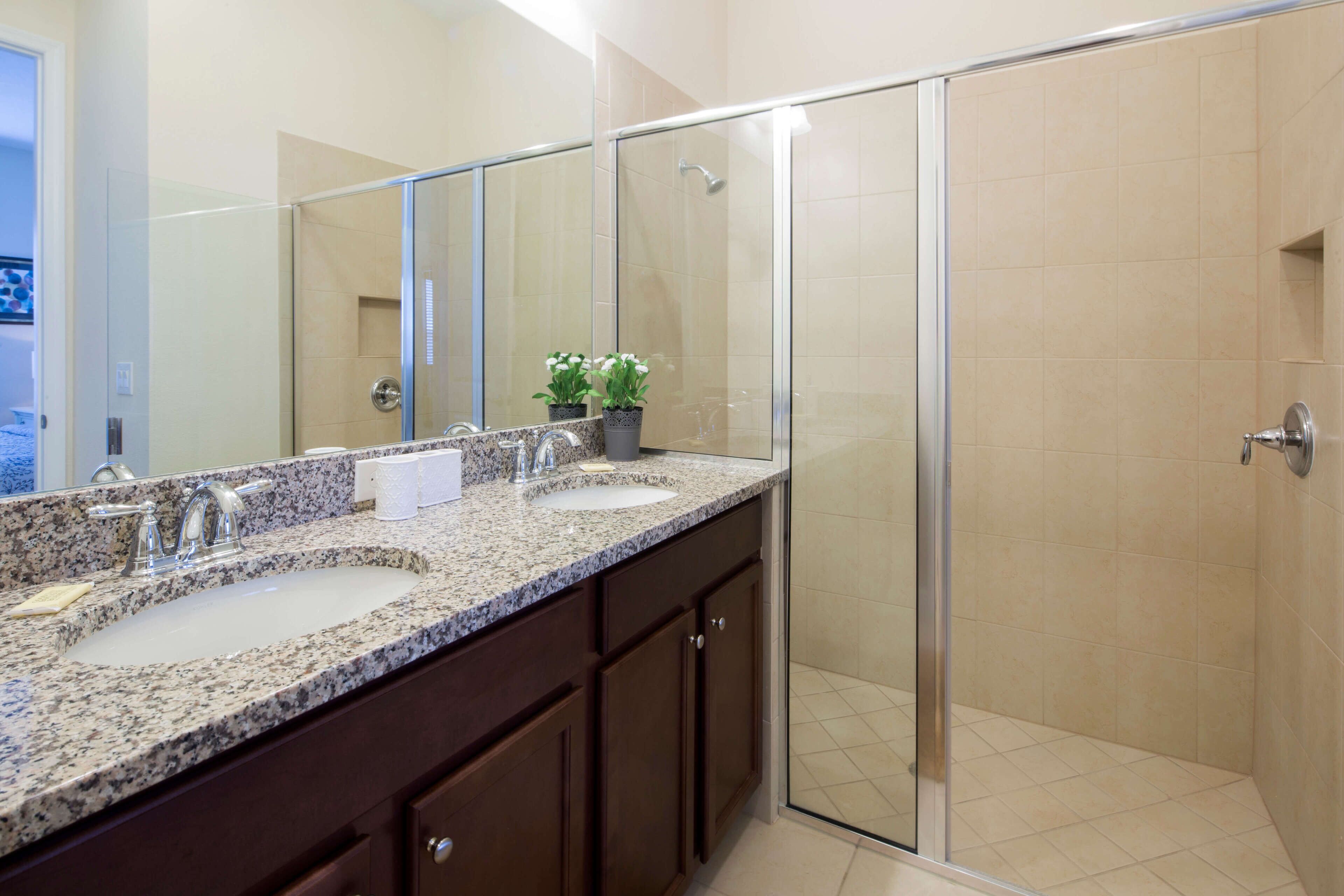 A bathroom with a granite countertop, two sinks, a large mirror, and a glass shower enclosure.