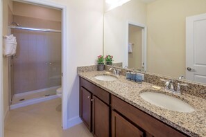 A bathroom with a shower, two sinks, a large mirror, and wooden cabinets.