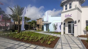 A modern building with a "Festival Welcome Center" sign, a paved walkway, and landscaped areas with palm trees and plants.