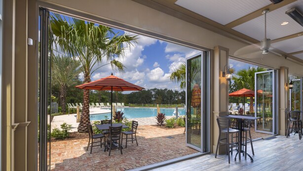 An indoor patio with a view of a swimming pool, outdoor seating, and palm trees.
