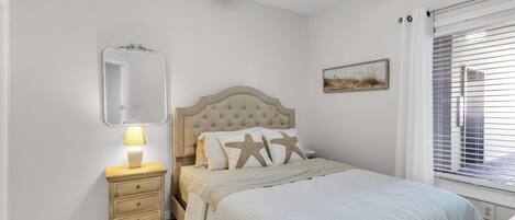 Un dormitorio con cama, mesita de noche, lámpara, ventilador de techo, ventana con persianas y espejo montado en la pared.