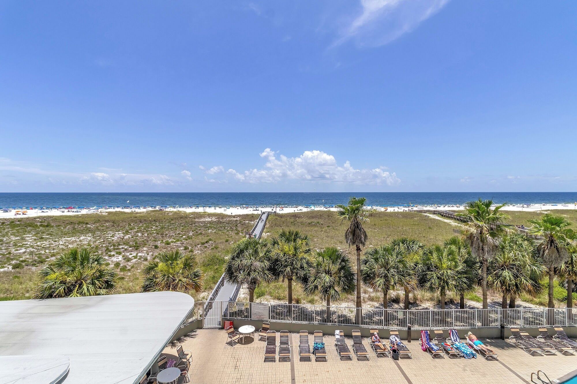Blick auf einen Strand mit Poolbereich, Liegestühlen und Palmen.