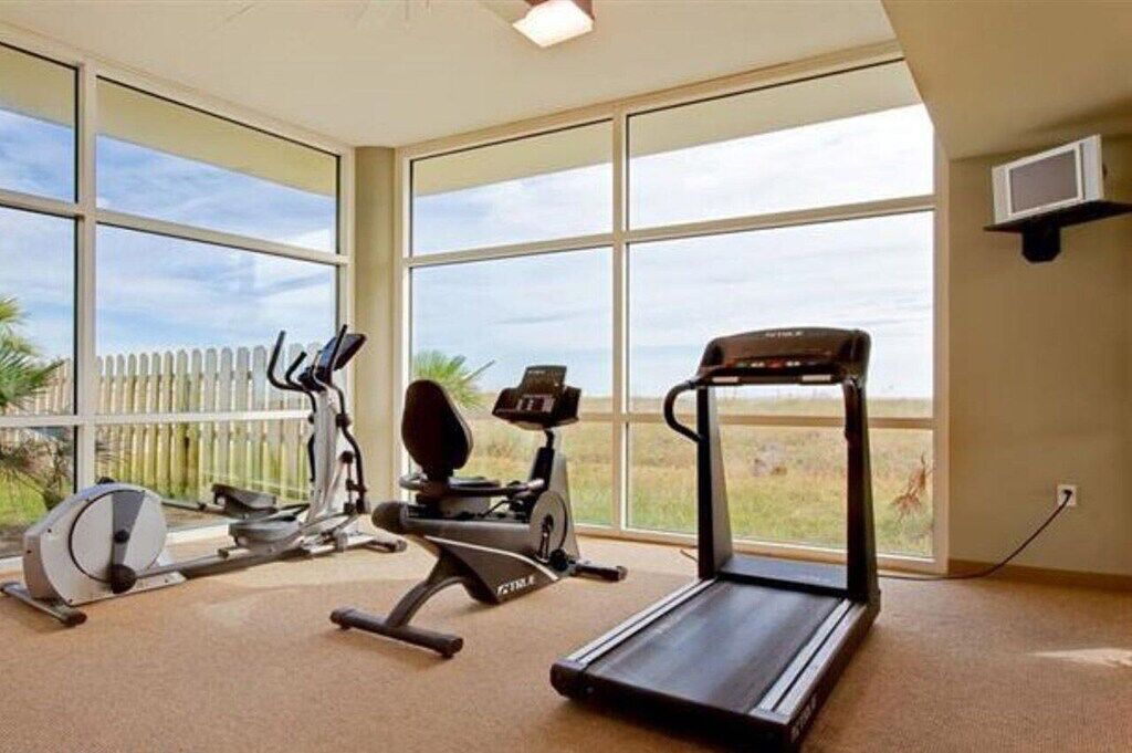A home gym with a treadmill, elliptical, and stationary bike, large windows with a view of the outdoors.