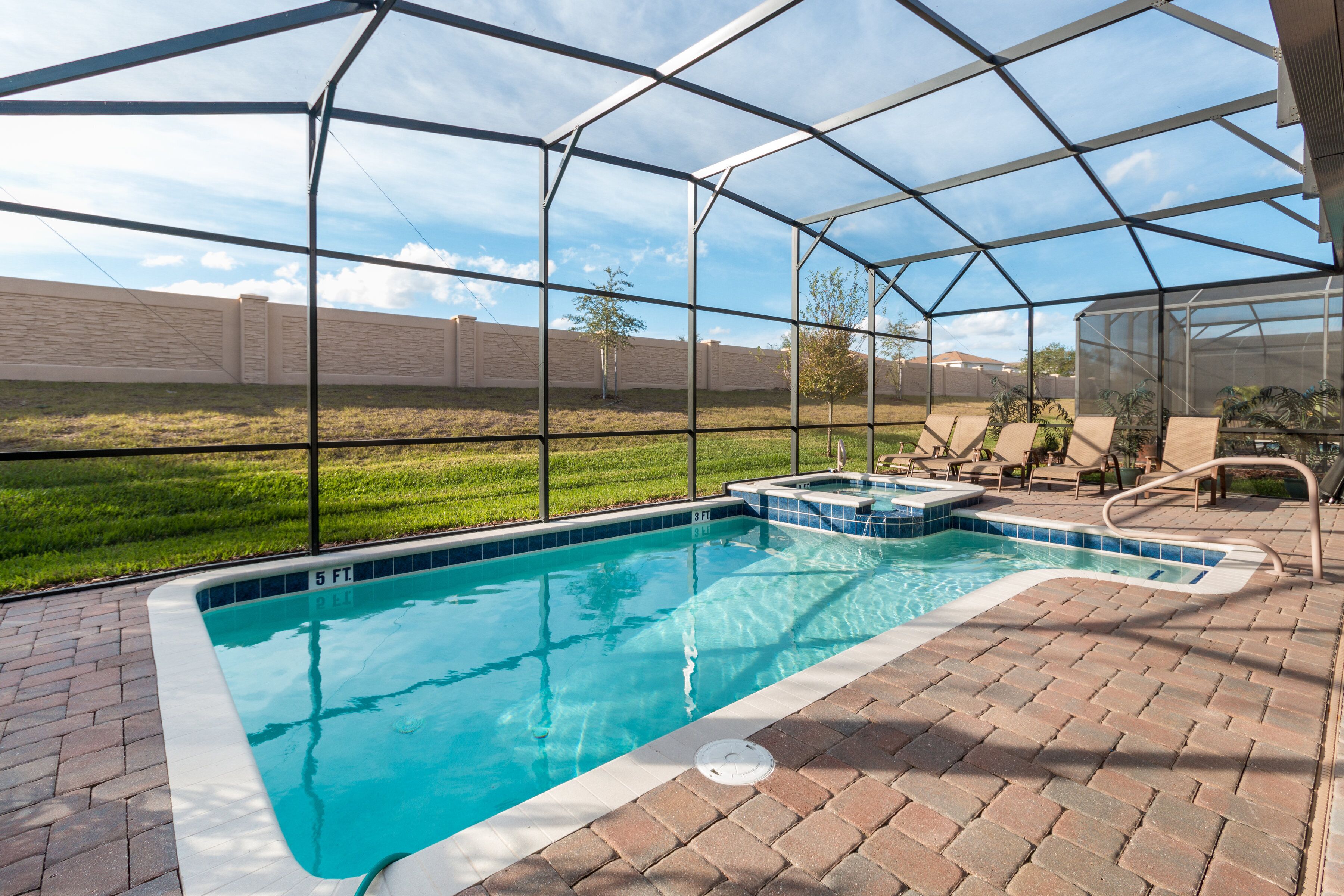 A swimming pool with a glass enclosure, surrounded by a brick patio and a grassy area.