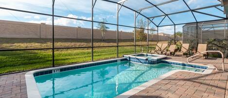 A swimming pool with a glass enclosure, surrounded by a brick patio and a grassy area.