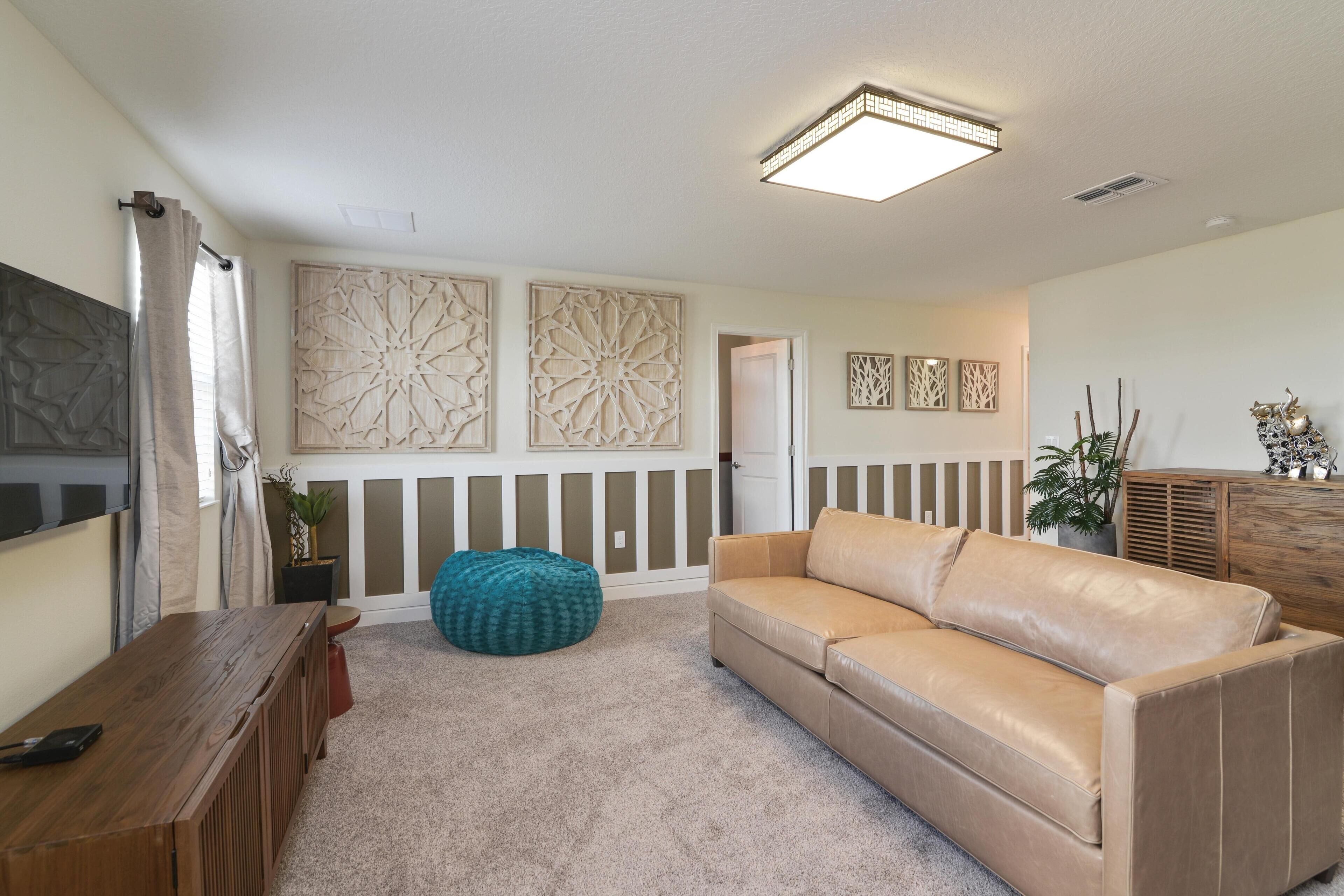 A living room with a beige leather sofa, a wooden coffee table, a teal bean bag, and decorative wall panels.